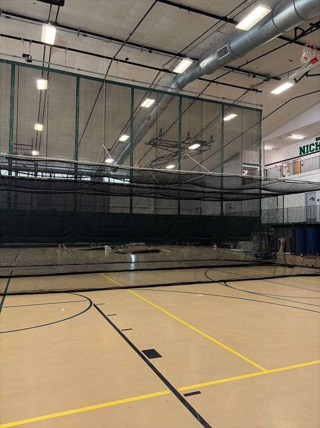 Motorized gymnasium equipment installation showing the overhead hoist system for a retractable batting cage at Nichols College.
