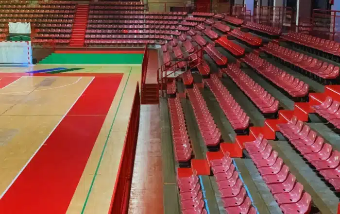 Bleacher inspection company examining gymnasium seating structure including bolts, railings, stairs, and load-bearing supports before public use approval